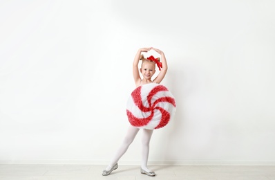 Image of Cute little girl dressed as candy near white wall. Christmas suit