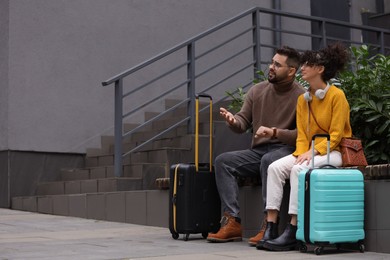 Photo of Being late. Worried couple with suitcases sitting on bench outdoors, space for text