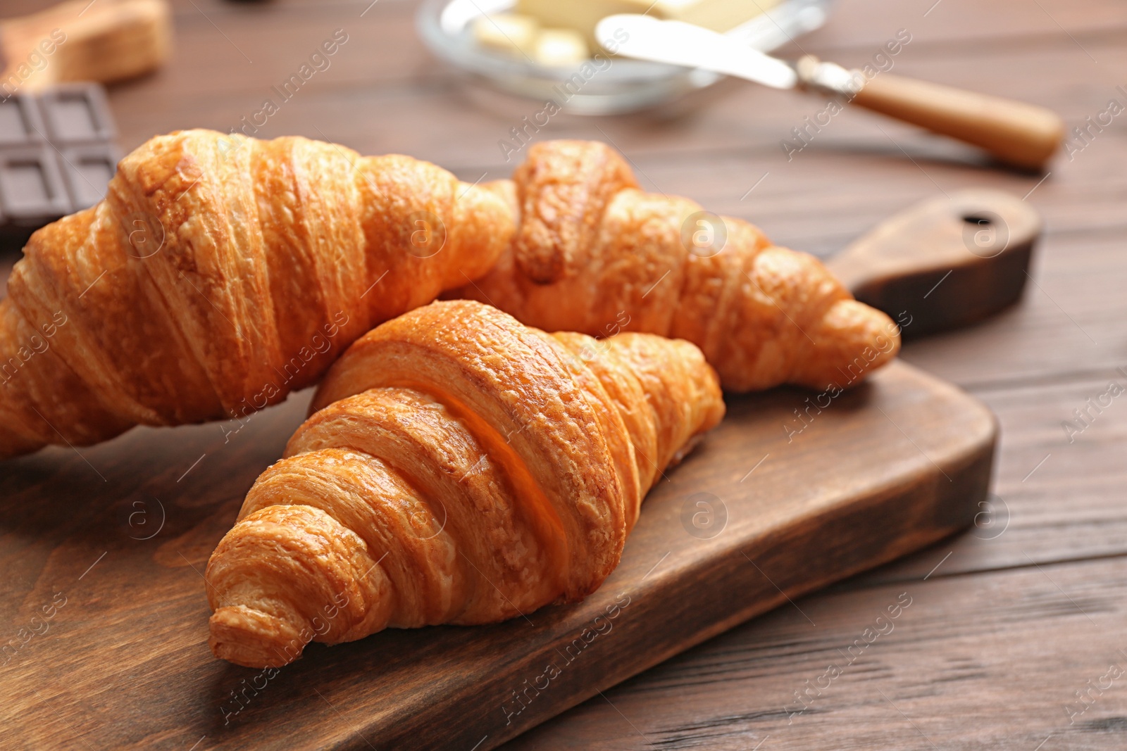 Photo of Board with tasty croissants on wooden table, closeup. French pastry