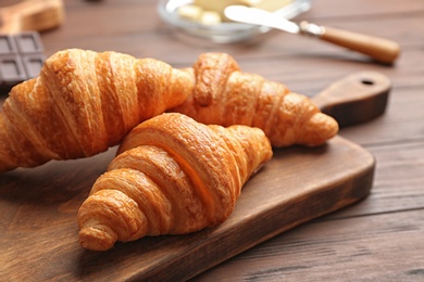 Photo of Board with tasty croissants on wooden table, closeup. French pastry
