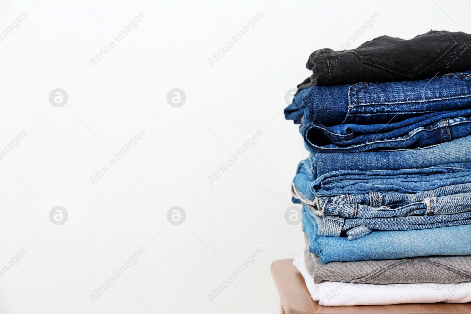 Photo of Stack of different jeans on table against white background. Space for text