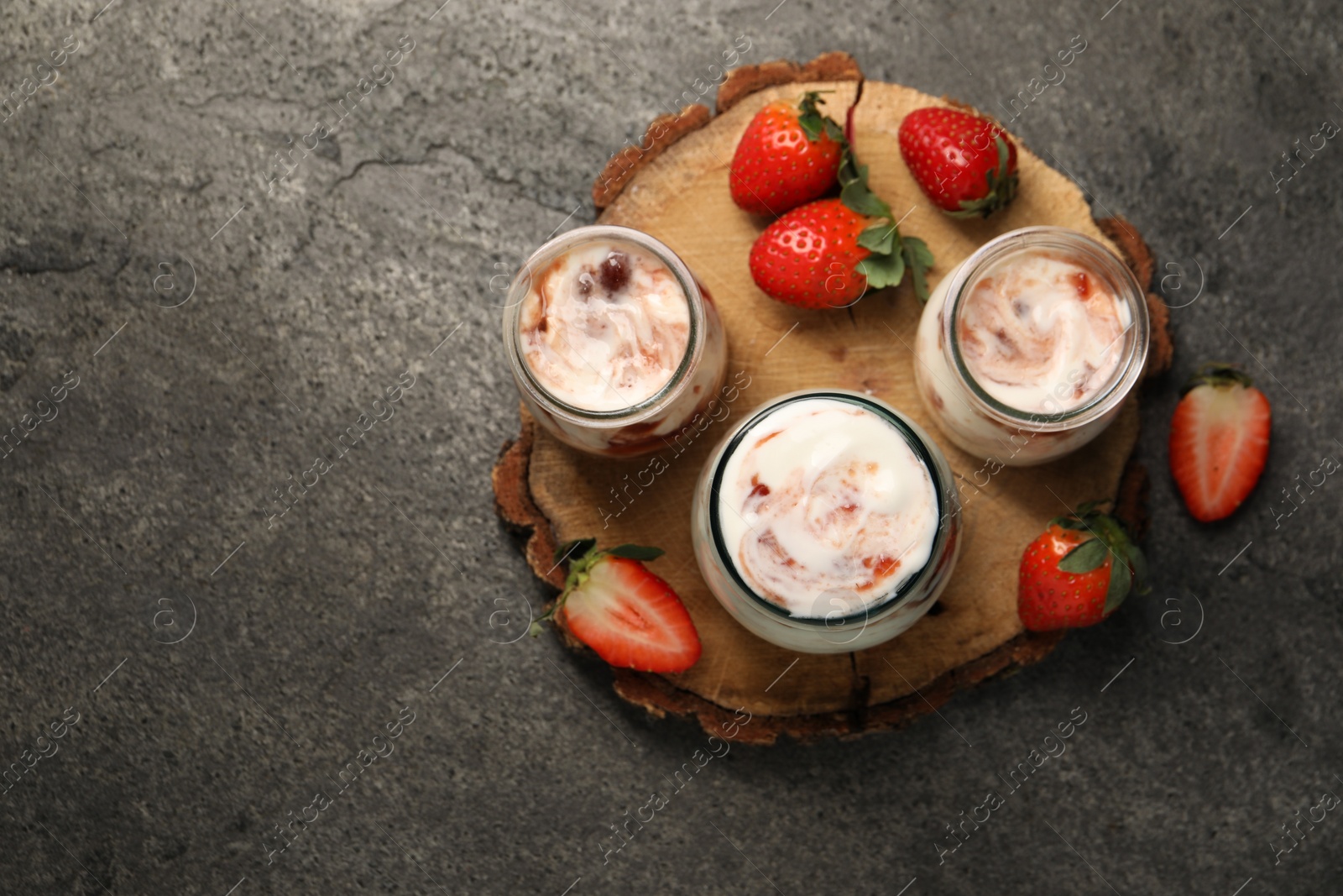 Photo of Tasty yoghurt with jam and strawberries on grey textured table, top view. Space for text