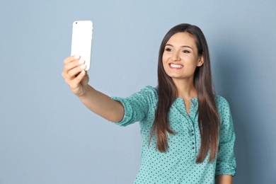 Young beautiful woman taking selfie against grey background