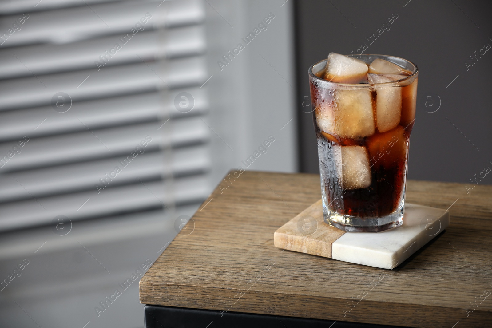 Photo of Glass of cold drink and stylish cup coaster on wooden table in room. Space for text