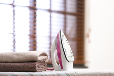 Photo of Modern iron and towels on board in room. Space for text