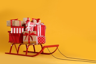 Photo of Sleigh with gift boxes on yellow background. Space for text