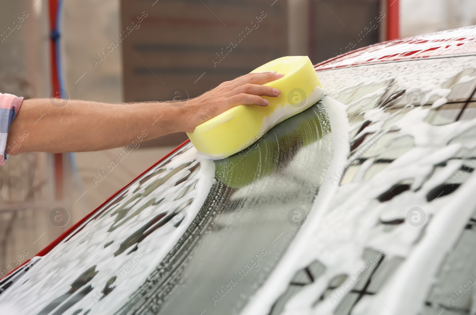 Photo of Man washing red auto with sponge at car wash, closeup