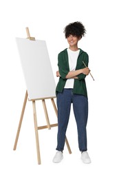 Photo of Young woman holding brush near easel with canvas against white background