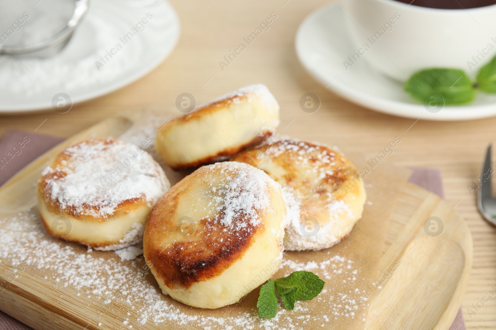 Photo of Delicious cottage cheese pancakes with sugar powder on wooden board, closeup