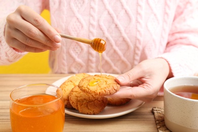 Photo of Woman pouring honey onto cookie at wooden table, closeup