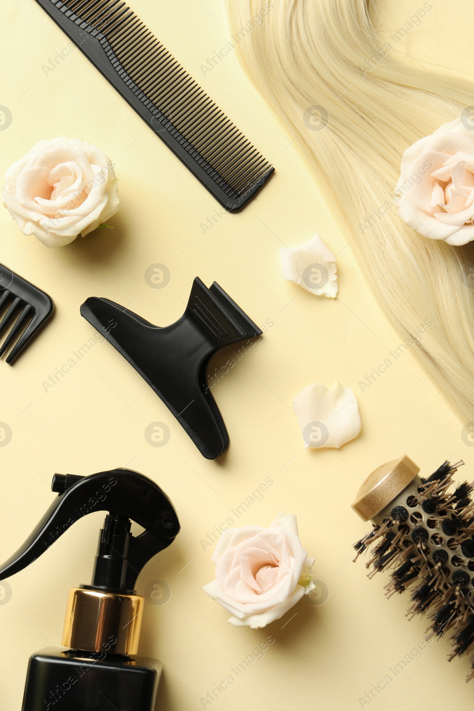 Photo of Flat lay composition with different hairdresser tools and flowers on pale yellow background