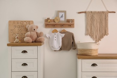 Photo of Wooden shelf with baby clothes, toys and furniture in room. Interior design