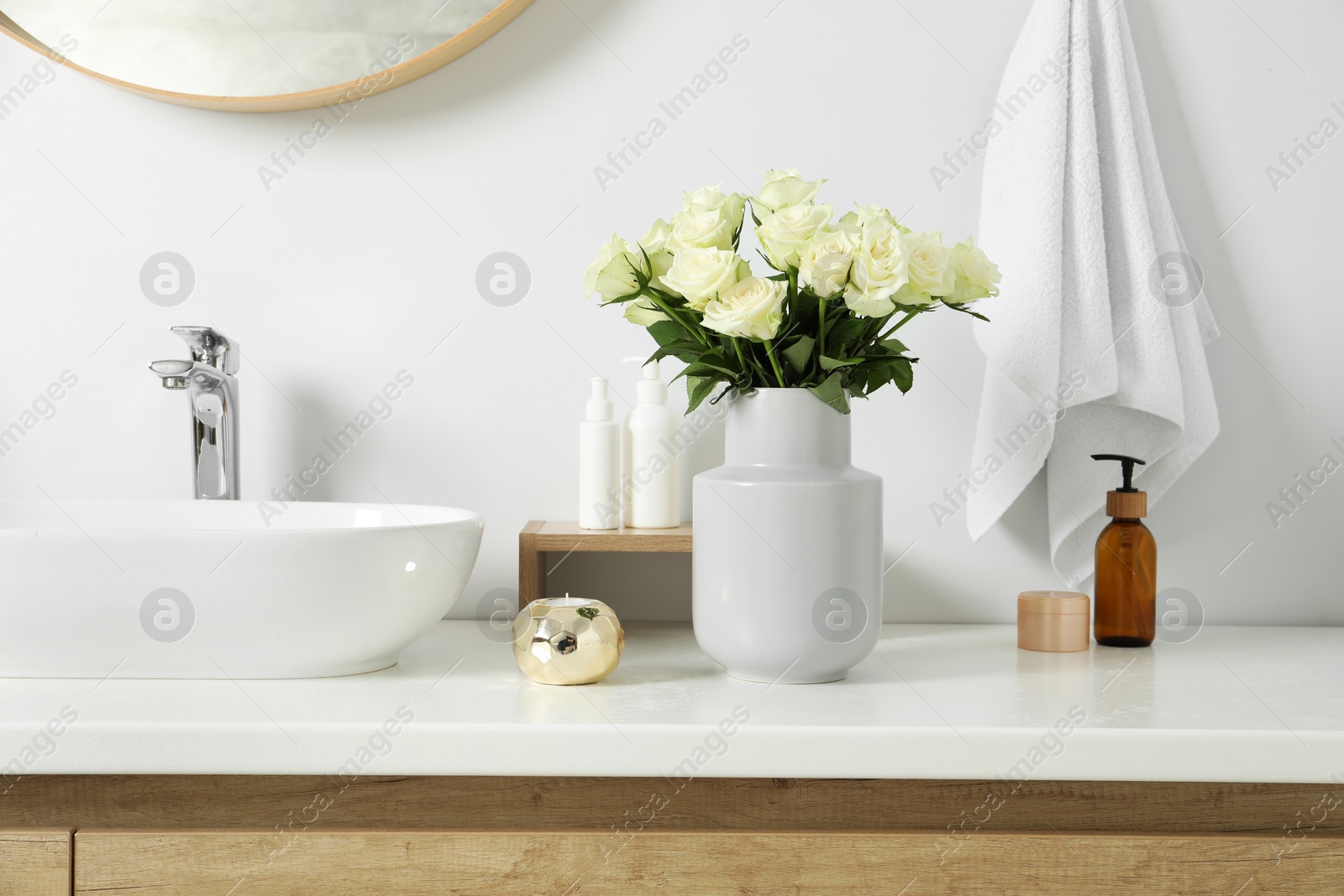 Photo of Vase with beautiful white roses and toiletries near sink in bathroom