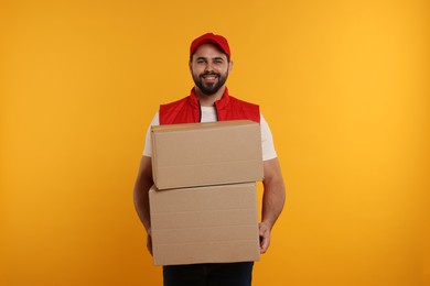 Happy young courier with parcels on orange background