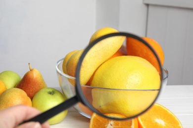 Photo of Woman with magnifying glass exploring lemons indoors, closeup. Poison detection