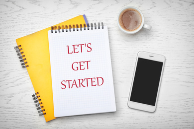 Notebook with phrase LET'S GET STARTED, smartphone and cup of coffee on white wooden background, flat lay