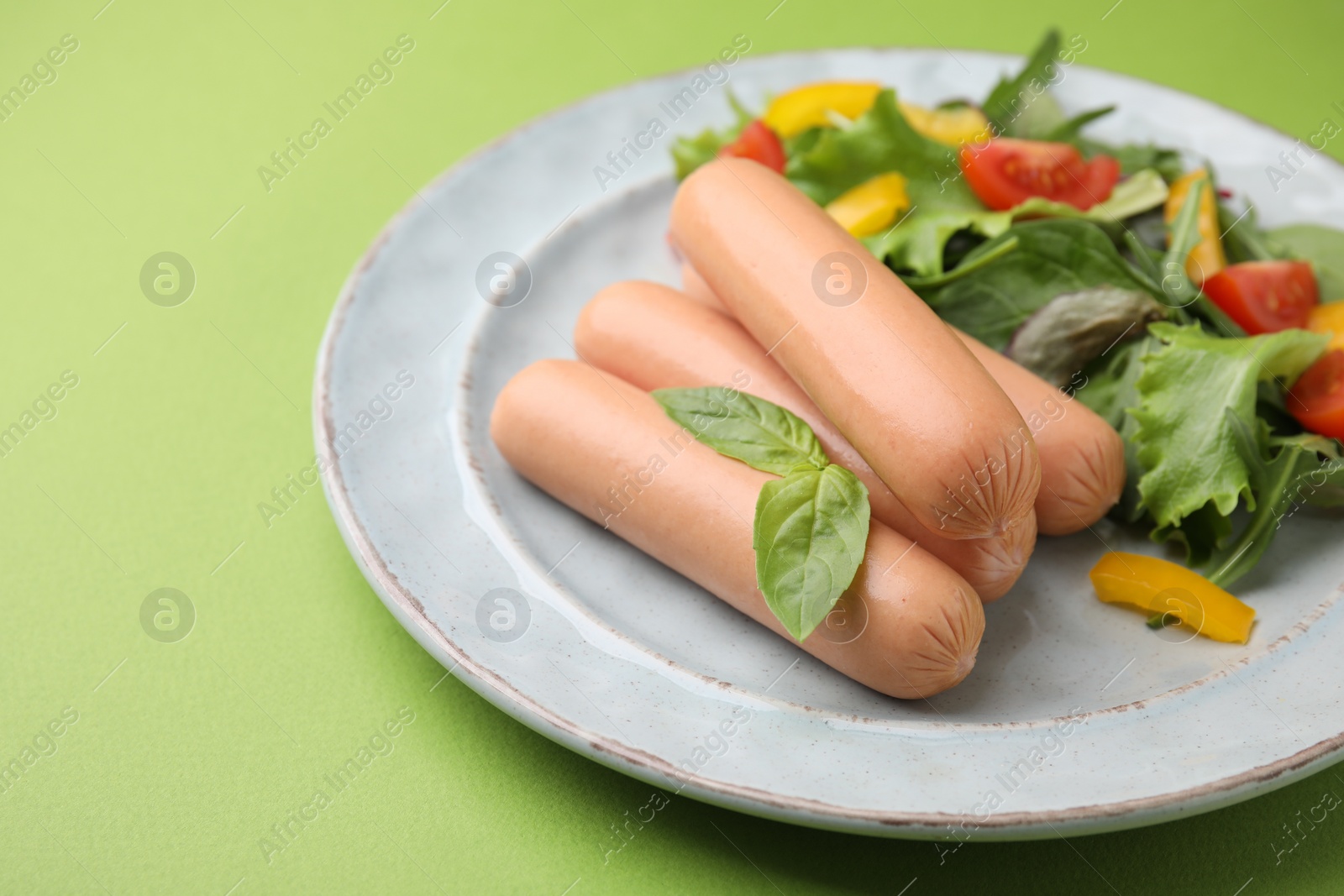 Photo of Delicious boiled sausages with salad on green