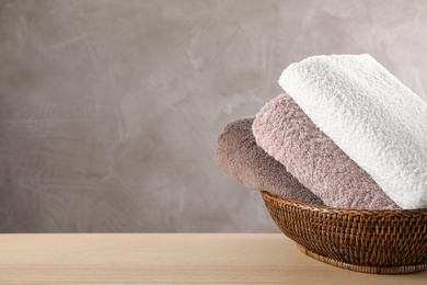 Wicker basket with folded bath towels on wooden table. Space for text