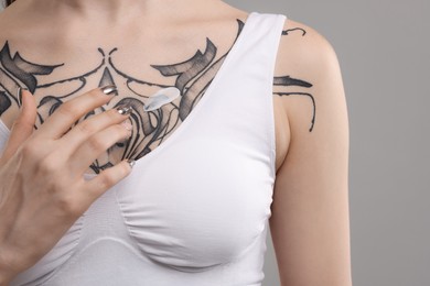 Photo of Woman applying healing cream onto her tattoos against grey background, closeup