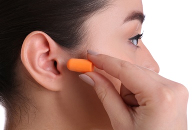 Young woman inserting foam ear plug on white background, closeup