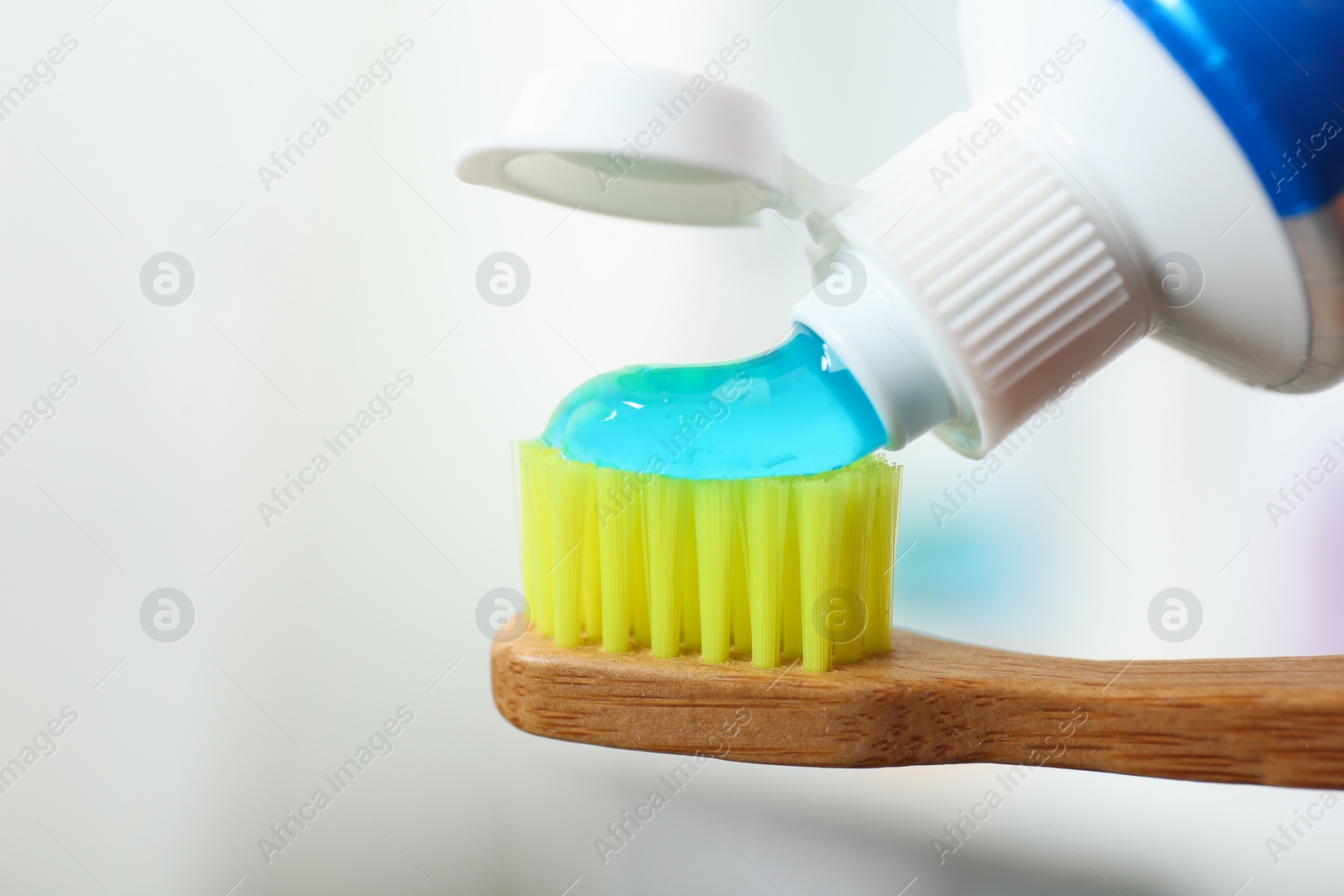 Photo of Applying toothpaste on brush against blurred background, closeup