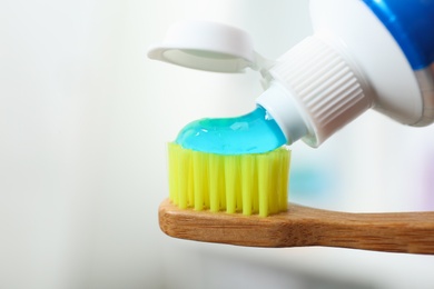 Photo of Applying toothpaste on brush against blurred background, closeup