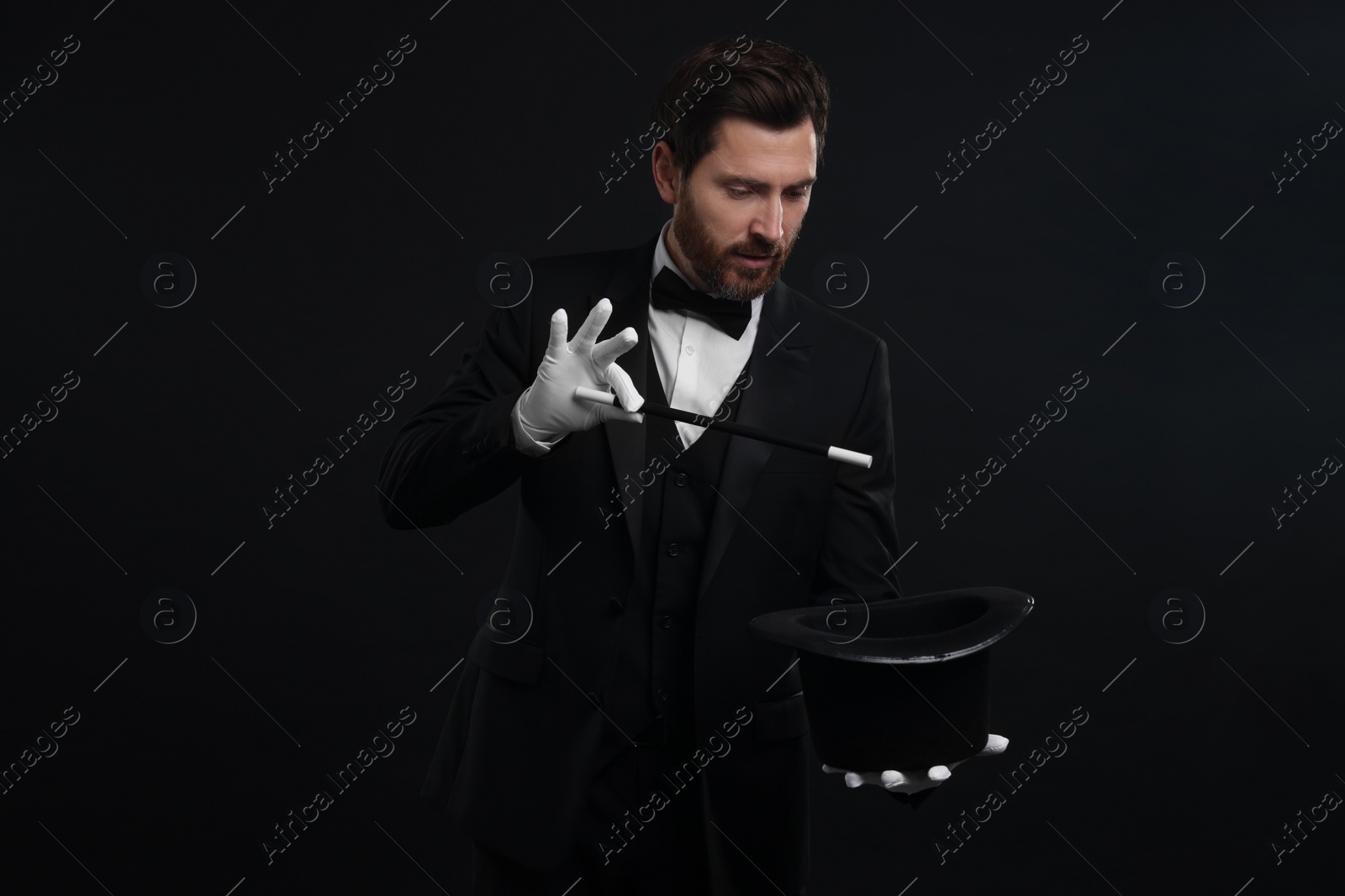Photo of Magician showing magic trick with top hat on black background