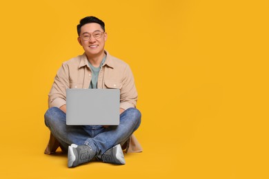 Photo of Happy man with laptop on yellow background, space for text