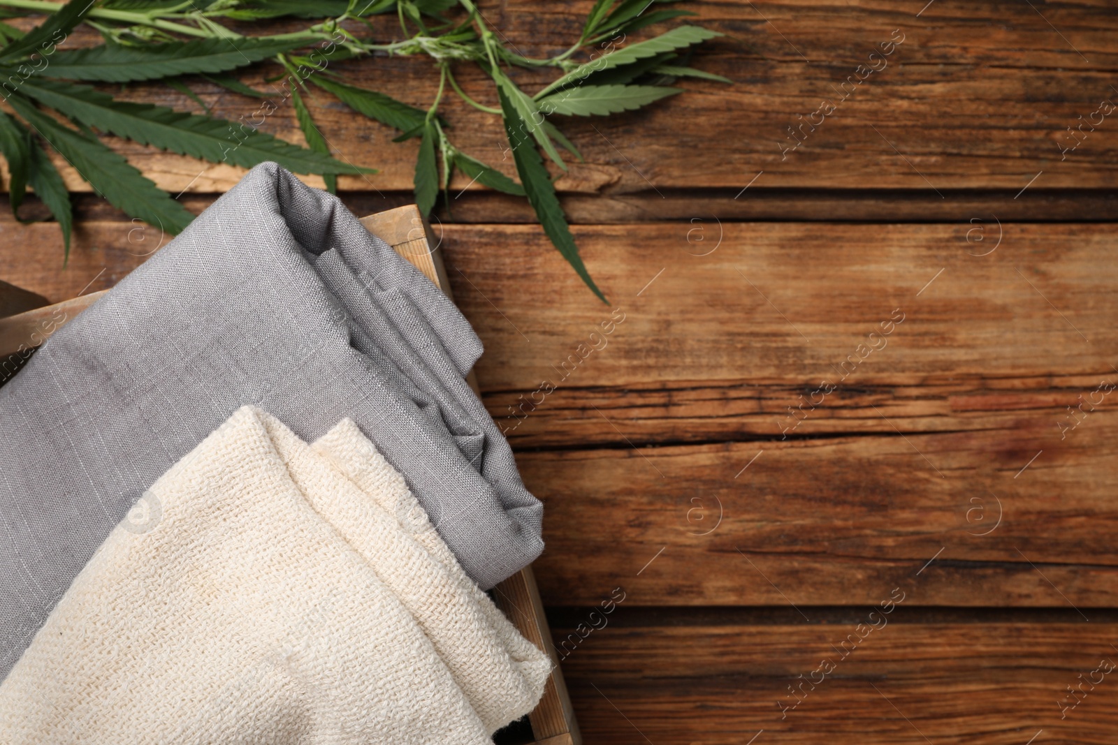 Photo of Hemp cloths  in crate and green leaves on wooden table, flat lay. Space for text