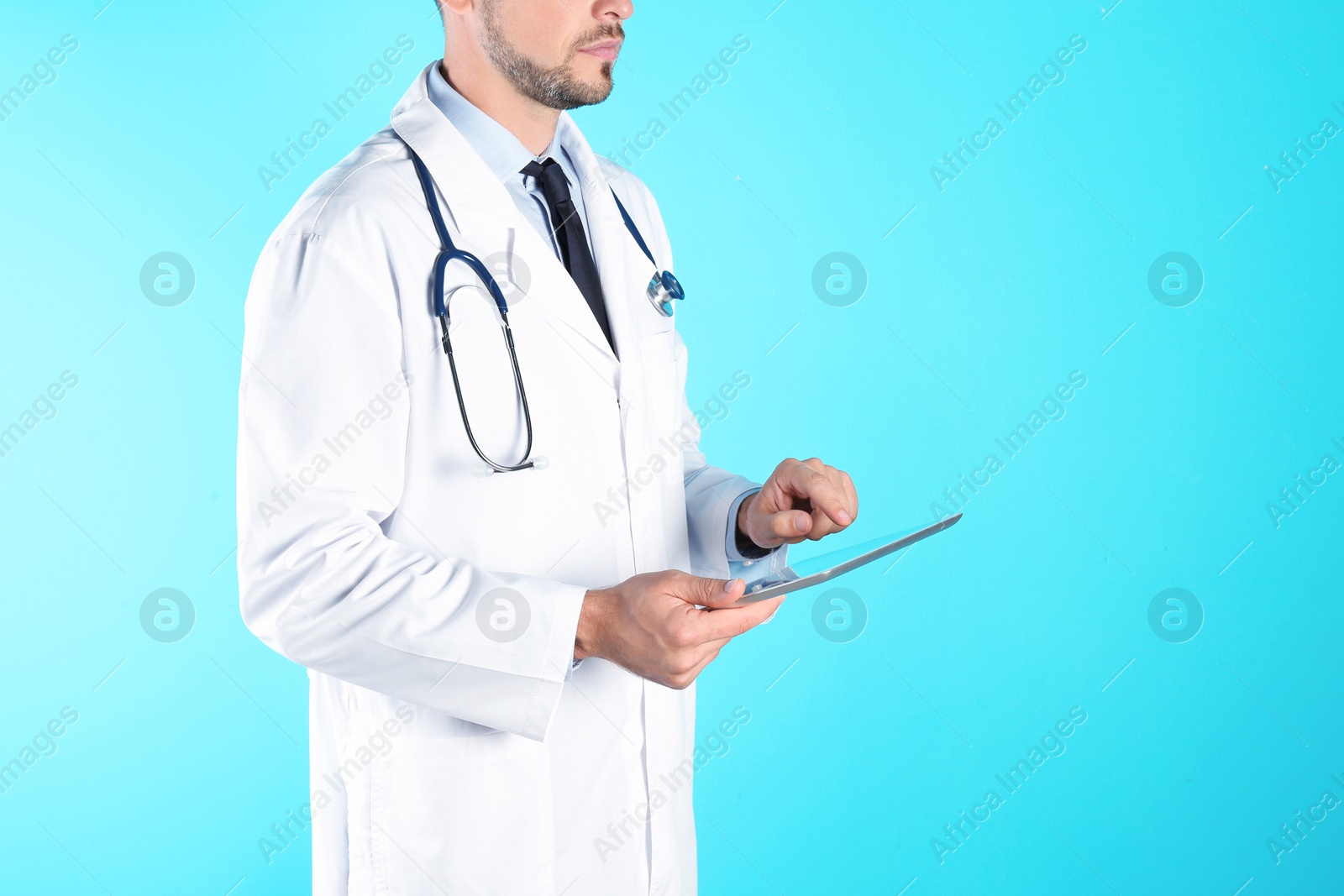 Photo of Male doctor holding modern tablet on color background, closeup with space for text