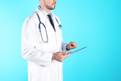 Male doctor holding modern tablet on color background, closeup with space for text