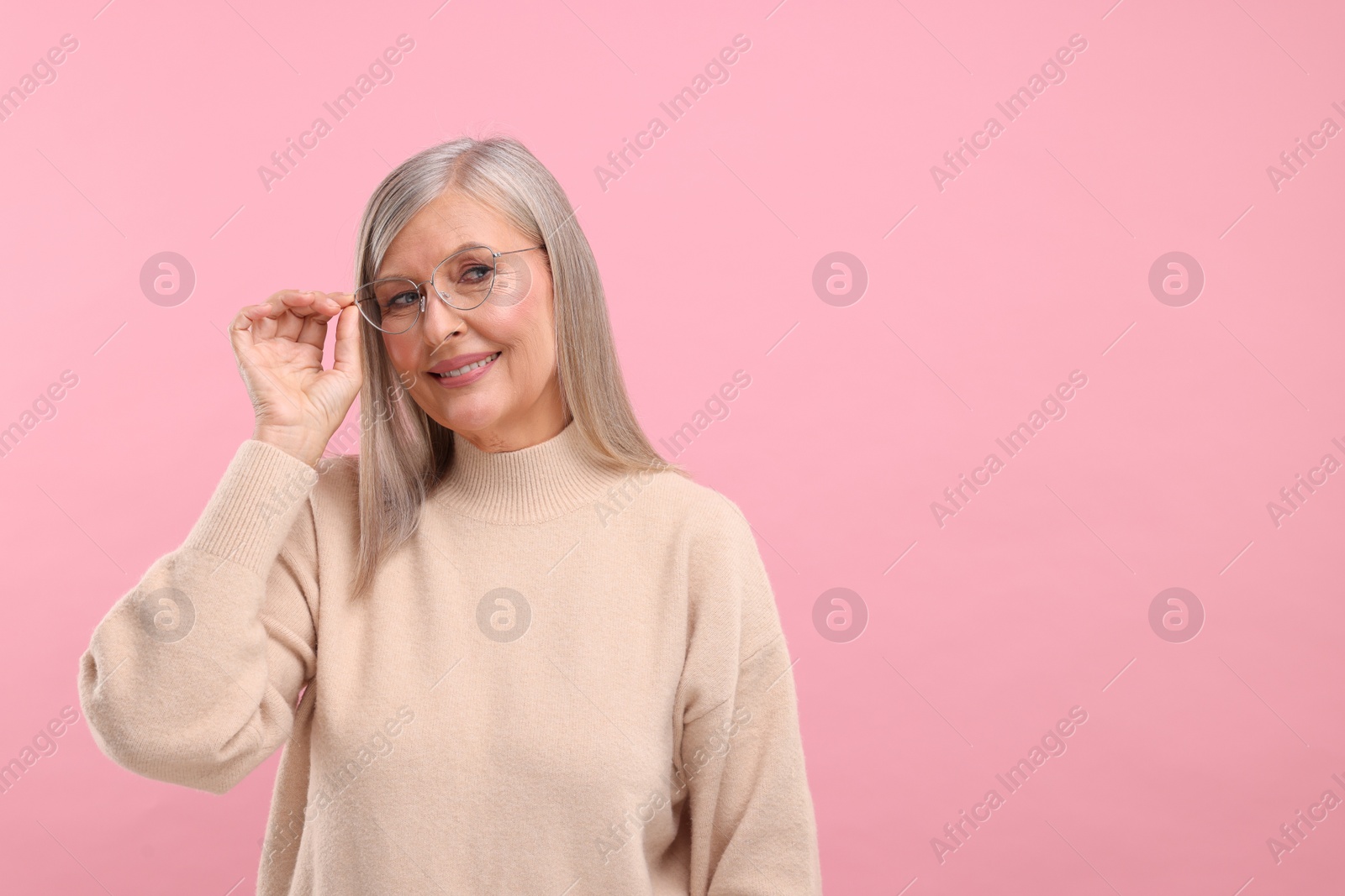 Photo of Portrait of beautiful middle aged woman in eyeglasses on pink background, space for text