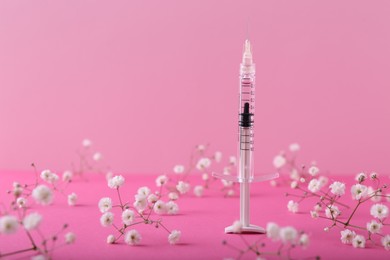 Cosmetology. Medical syringe and gypsophila flowers on pink background, space for text