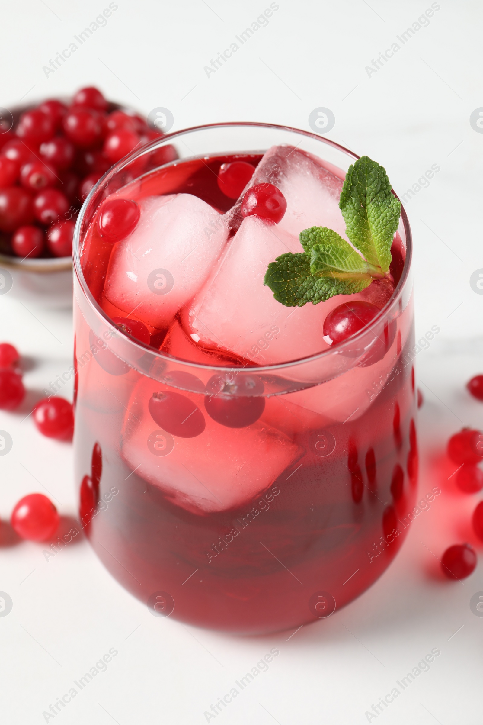 Photo of Tasty cranberry juice with ice cubes in glass and fresh berries on white wooden table, closeup