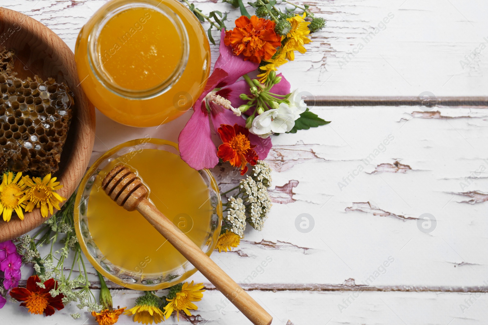 Photo of Delicious honey with combs and different flowers on white wooden table, flat lay. Space for text