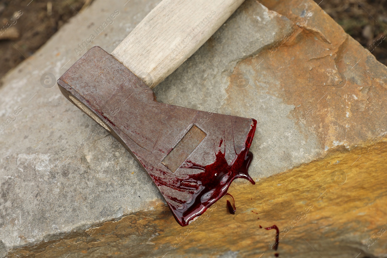 Photo of Axe with blood on stone outdoors, top view