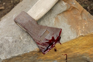 Axe with blood on stone outdoors, top view