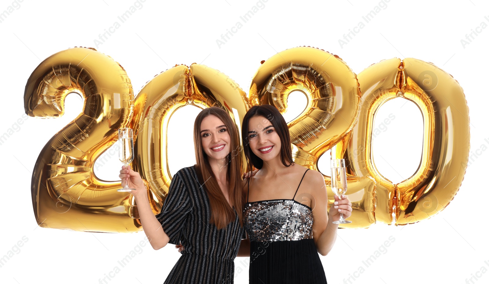 Photo of Happy young women with glasses of champagne near golden 2020 balloons on white background. New Year celebration