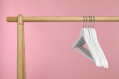 Photo of White clothes hangers on wooden rack against pink background