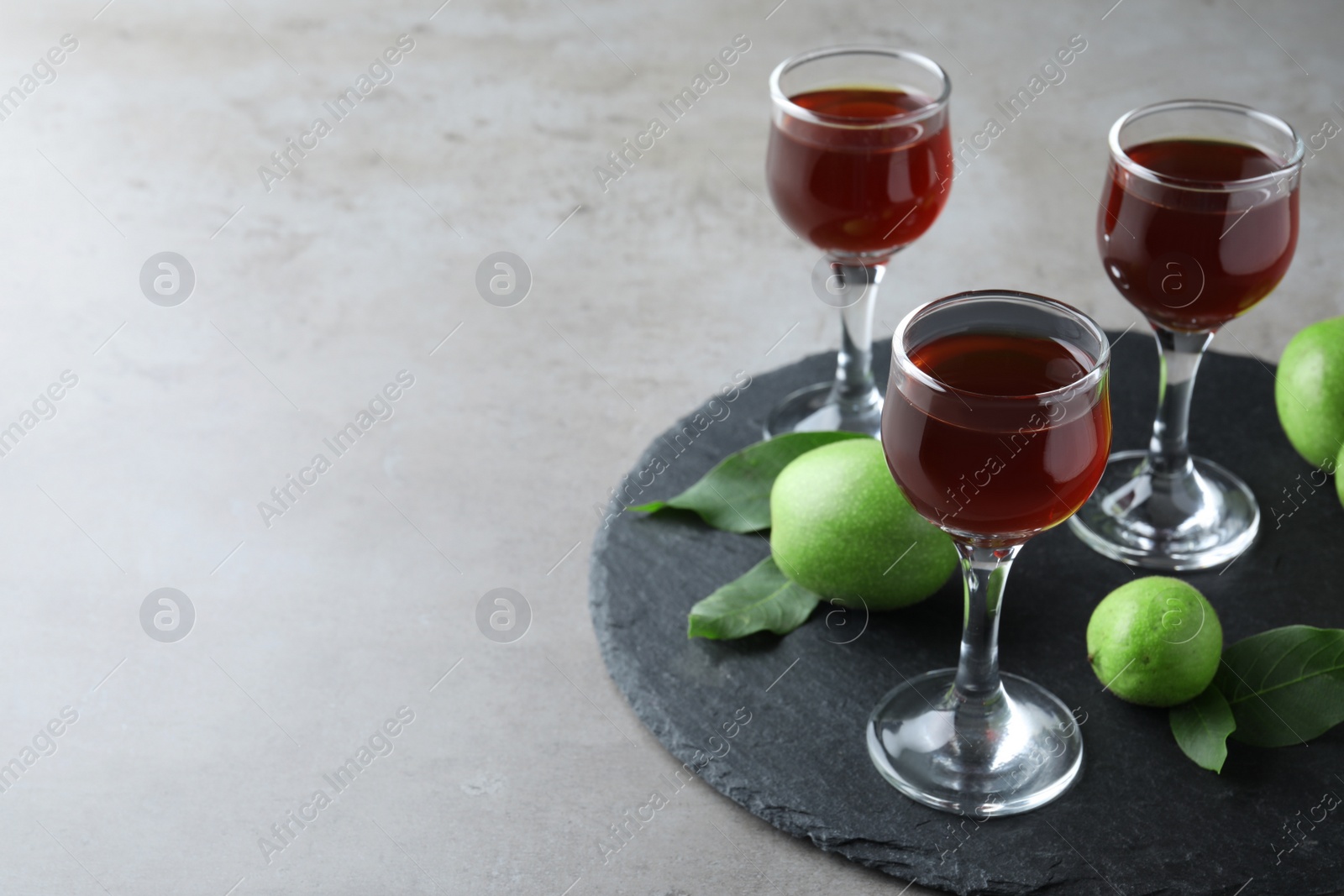 Photo of Delicious liqueur and green walnuts on grey table. Space for text