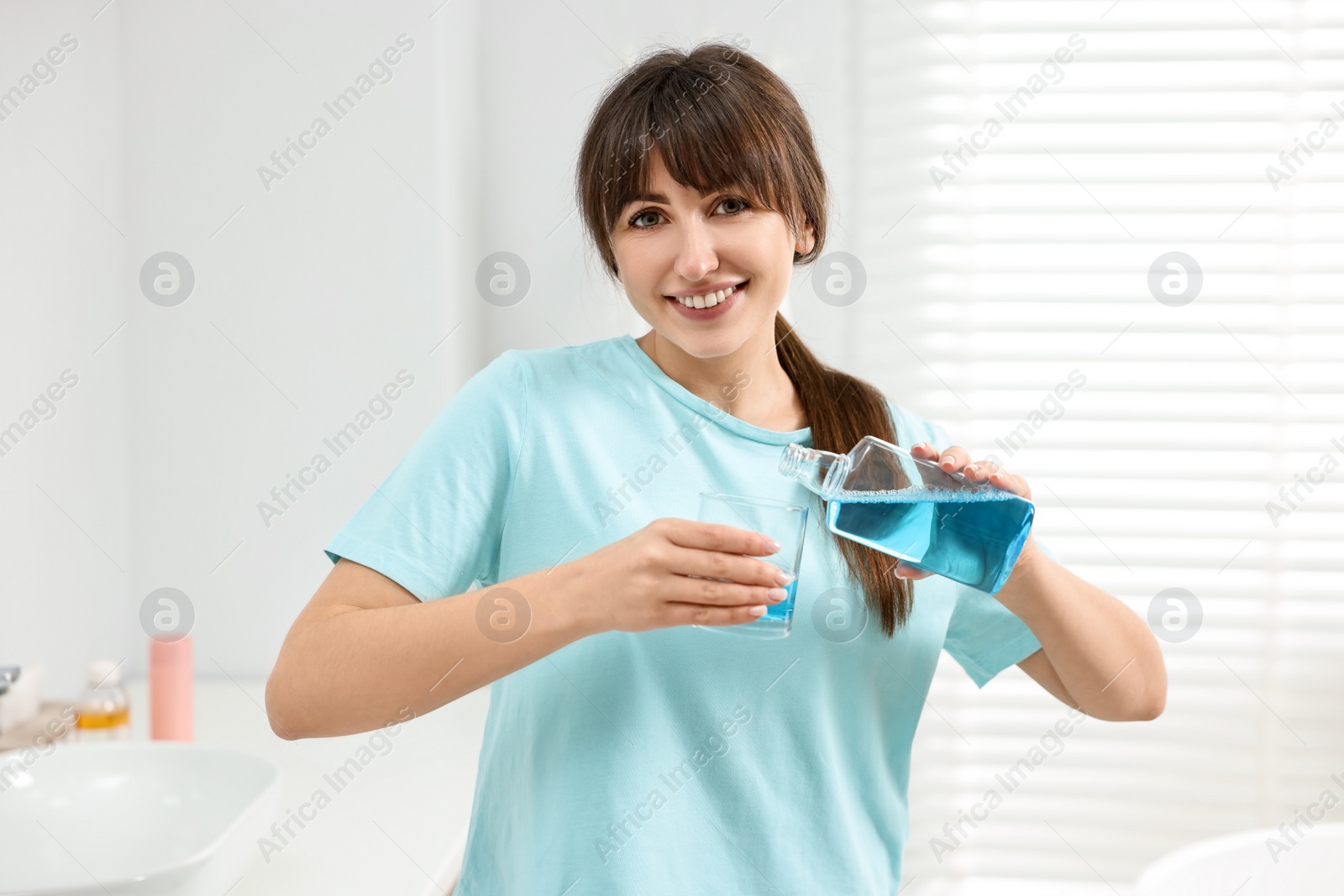 Photo of Young woman using mouthwash in bathroom. Oral hygiene