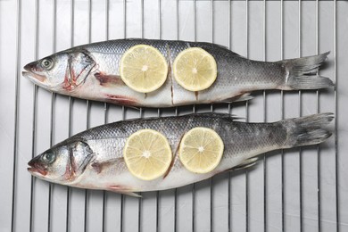 Photo of Oven rack with raw sea bass fish and lemon on light grey table, top view