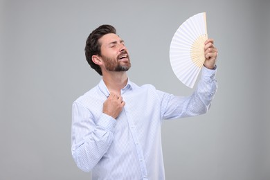 Happy man holding hand fan on light grey background