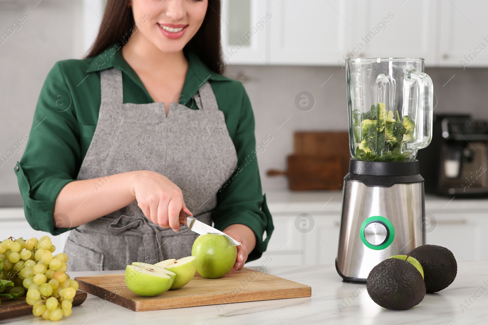 Photo of Young woman cutting apple for smoothie at white table in kitchen, closeup