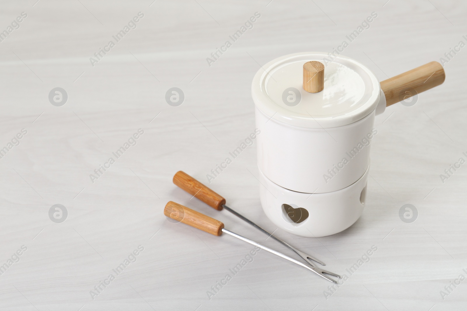 Photo of Fondue set on white wooden table. Space for text