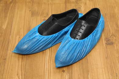 Men`s black shoes in blue shoe covers on wooden floor