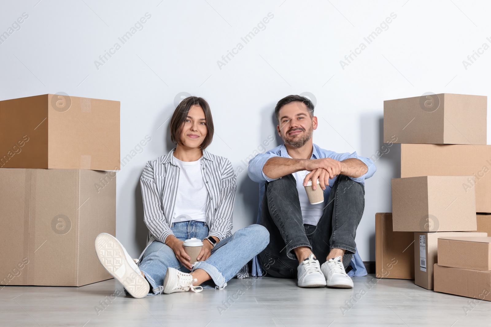 Photo of Happy couple with takeaway coffee resting on floor in new apartment. Moving day