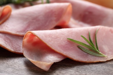 Photo of Slices of delicious ham and rosemary on wooden table, closeup