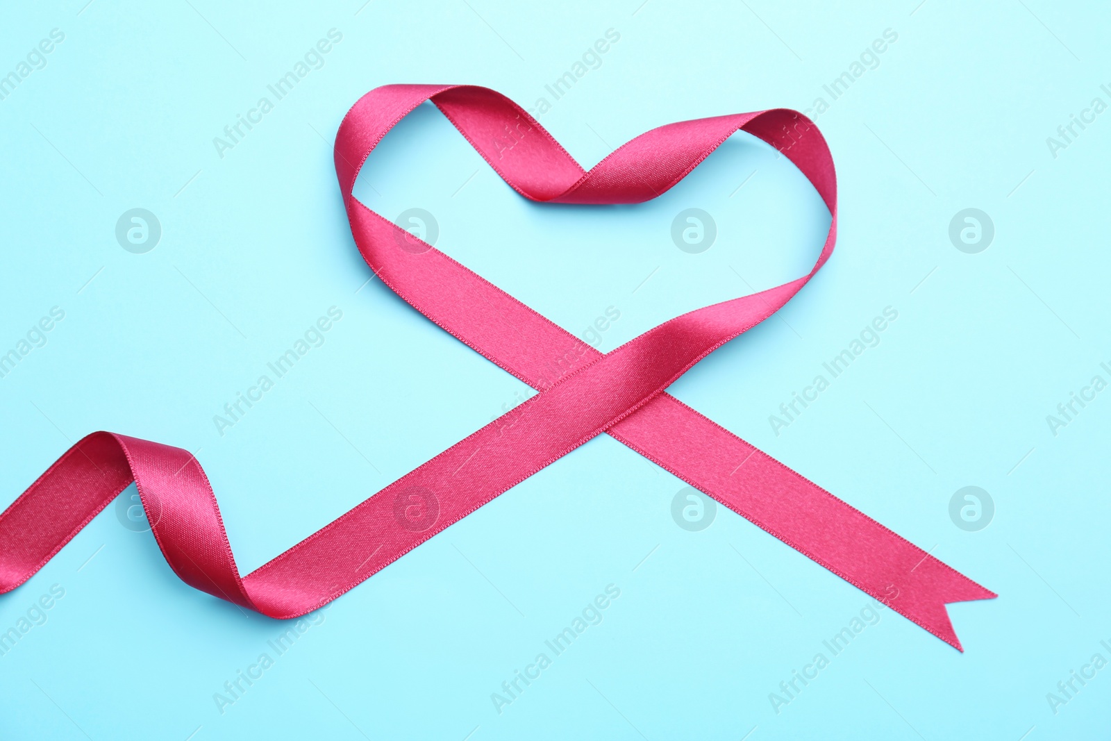 Photo of Heart made of pink ribbon on color background, top view