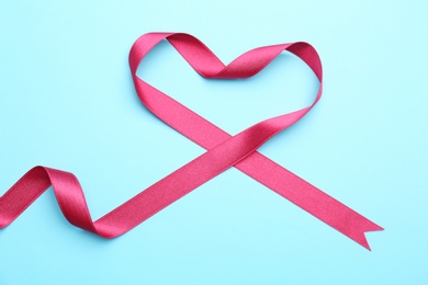 Heart made of pink ribbon on color background, top view